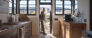 Movie still from “Windfall” (2022), directed by Charlie McDowell – A man standing in front of an open window; Wide shot, Over the shoulder angle