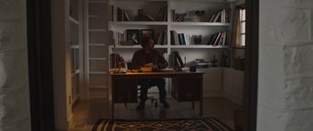 Movie still from “Windfall” (2022), directed by Charlie McDowell – A man sitting at a desk in front of a book shelf; Wide shot, High angle