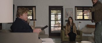 Movie still from “Windfall” (2022), directed by Charlie McDowell – A woman sitting on a chair in a living room; Wide shot, Over the shoulder angle