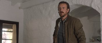 Movie still from “Windfall” (2022), directed by Charlie McDowell – A man standing in a room with a wall behind him; Medium shot, Low angle
