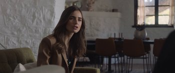 Movie still from “Windfall” (2022), directed by Charlie McDowell – A beautiful young lady sitting in a room; Medium shot, Over the shoulder angle