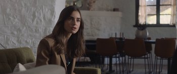 Movie still from “Windfall” (2022), directed by Charlie McDowell – A beautiful young lady sitting in a room; Medium shot, Over the shoulder angle