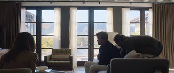 Movie still from “Windfall” (2022), directed by Charlie McDowell – A man and a woman sitting on a couch in front of a window; Wide shot, Over the shoulder angle