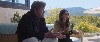 Movie still from “Windfall” (2022), directed by Charlie McDowell – A man and a woman sitting next to each other on a couch; Medium shot, Over the shoulder angle