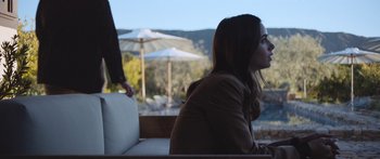 Movie still from “Windfall” (2022), directed by Charlie McDowell – A woman sitting on top of a white bench; Medium shot, Over the shoulder angle
