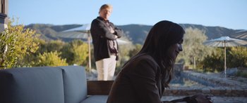 Movie still from “Windfall” (2022), directed by Charlie McDowell – A man and a woman standing in front of an umbrella; Wide shot, Over the shoulder angle
