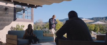 Movie still from “Windfall” (2022), directed by Charlie McDowell – A man standing on a porch with two other people; Wide shot, Over the shoulder angle