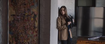 Movie still from “Windfall” (2022), directed by Charlie McDowell – A woman in a brown coat holding a camera; Medium shot, Low angle