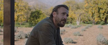 Movie still from “Windfall” (2022), directed by Charlie McDowell – A man with a beard is sitting in the dirt; Close Up shot, Over the shoulder angle