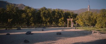 Movie still from “Windfall” (2022), directed by Charlie McDowell – A man standing in a field with trees in the background; Extreme Wide shot, High angle