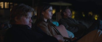 Movie still from “Windfall” (2022), directed by Charlie McDowell – A woman sitting in front of two other people; Medium shot, Over the shoulder angle