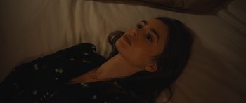 Movie still from “Windfall” (2022), directed by Charlie McDowell – A woman laying on a bed with her eyes closed; Close Up shot, High angle