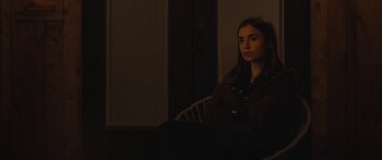 Movie still from “Windfall” (2022), directed by Charlie McDowell – A woman sitting in a chair in a dark room; Medium shot, Over the shoulder angle