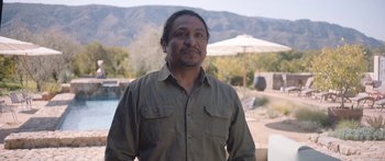 Movie still from “Windfall” (2022), directed by Charlie McDowell – A man standing in front of an outdoor setting; Medium shot, Over the shoulder angle