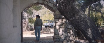 Movie still from “Windfall” (2022), directed by Charlie McDowell – A man standing under an arch near a tree; Wide shot, Over the shoulder angle