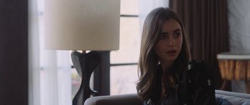 Movie still from “Windfall” (2022), directed by Charlie McDowell – A woman sitting on a couch in front of a window; Medium shot, Over the shoulder angle