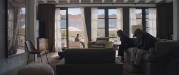 Movie still from “Windfall” (2022), directed by Charlie McDowell – Two people are sitting in a living room with a view; Wide shot, Over the shoulder angle