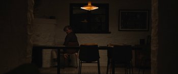 Movie still from “Windfall” (2022), directed by Charlie McDowell – A person sitting at a table in a dark room; Wide shot, High angle