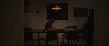 Movie still from “Windfall” (2022), directed by Charlie McDowell – A person sitting at a table in a dark room; Wide shot, Low angle