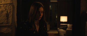 Movie still from “Windfall” (2022), directed by Charlie McDowell – A woman with long hair is standing in the dark; Medium shot, Over the shoulder angle