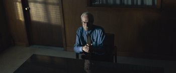 Movie still from “Wormwood” (2017), directed by Errol Morris – An older man sitting at a table in front of a window; Medium shot, Low angle