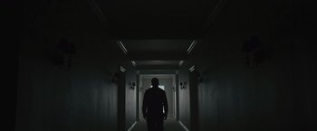 Movie still from “Wormwood” (2017), directed by Errol Morris – A man standing in a dark hallway looking at the light; Wide shot, Low angle