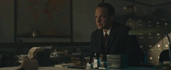Movie still from “Wormwood” (2017), directed by Errol Morris – A man sitting at a table in a suit and tie; Medium shot, Low angle