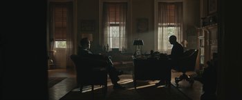 Movie still from “Wormwood” (2017), directed by Errol Morris – A man sitting on a chair in a living room; Wide shot, Low angle