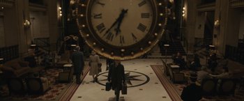 Movie still from “Wormwood” (2017), directed by Errol Morris – A group of people walking in front of a large clock; Wide shot, High angle