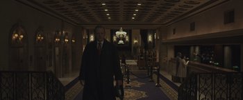 Movie still from “Wormwood” (2017), directed by Errol Morris – A man in a suit and tie walking down a hall way; Wide shot, Low angle