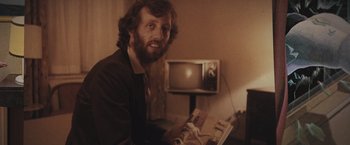 Movie still from “Wormwood” (2017), directed by Errol Morris – A man sitting in front of a tv and looking at the camera; Close Up shot, Low angle