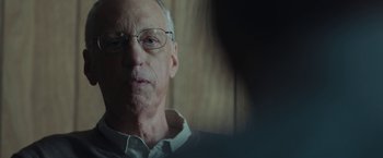 Movie still from “Wormwood” (2017), directed by Errol Morris – An older man wearing glasses looking at the camera; Close Up shot, Over the shoulder angle