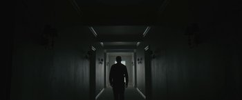 Movie still from “Wormwood” (2017), directed by Errol Morris – A man standing in a dark hallway looking at a window; Wide shot, Low angle