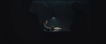 Movie still from “Wormwood” (2017), directed by Errol Morris – A man sitting at a table in a dark room; Wide shot, Over the shoulder angle