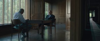 Movie still from “Wormwood” (2017), directed by Errol Morris – A man sitting at a table in front of a window; Wide shot, Low angle