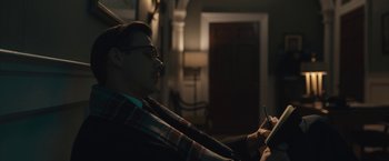 Movie still from “Wormwood” (2017), directed by Errol Morris – A man sitting in front of an open door looking at his cell phone; Medium shot, Over the shoulder angle