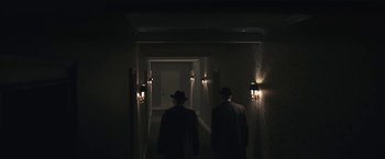 Movie still from “Wormwood” (2017), directed by Errol Morris – A couple of men walking down a hall way in the dark; Wide shot, High angle