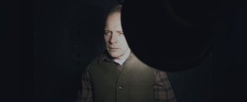 Movie still from “Wormwood” (2017), directed by Errol Morris – A man in a brown plaid shirt and a green vest; Close Up shot, Over the shoulder angle