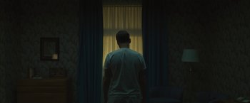 Movie still from “Wormwood” (2017), directed by Errol Morris – A man standing in front of a window in a room; Medium shot, Low angle