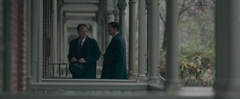 Movie still from “Wormwood” (2017), directed by Errol Morris – Two men in suits are standing in front of a pillar; Medium shot, Low angle