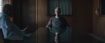 Movie still from “Wormwood” (2017), directed by Errol Morris – An older man sitting at a table in front of a mirror; Medium shot, Low angle