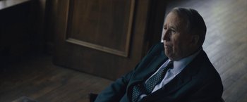 Movie still from “Wormwood” (2017), directed by Errol Morris – An older man wearing a suit and tie sitting in a chair; Close Up shot, Over the shoulder angle