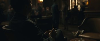 Movie still from “Wormwood” (2017), directed by Errol Morris – A man sitting in front of a group of people in a dark room; Medium shot, Over the shoulder angle