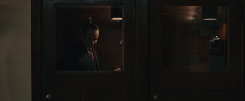 Movie still from “Wormwood” (2017), directed by Errol Morris – A man in a suit looking at his cell phone; Medium shot, Low angle