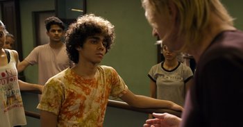 Movie still from “Yeh Ballet” (2020), directed by Sooni Taraporevala – A young man with curly hair talking to a group of young people; Medium shot, Over the shoulder angle