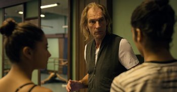 Movie still from “Yeh Ballet” (2020), directed by Sooni Taraporevala – A man with long blonde hair standing in front of two other men; Medium shot, Over the shoulder angle