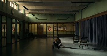 Movie still from “Yeh Ballet” (2020), directed by Sooni Taraporevala – A man sitting on the ground in a room; Extreme Wide shot, High angle