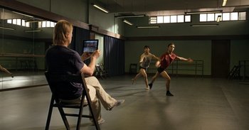 Movie still from “Yeh Ballet” (2020), directed by Sooni Taraporevala – A man sitting on a chair in front of two dancers; Wide shot, Low angle