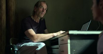 Movie still from “Yeh Ballet” (2020), directed by Sooni Taraporevala – A man sitting at a desk in a dark room; Medium shot, Low angle
