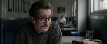 Movie still from “tick, tick... BOOM!” (2021), directed by Lin-Manuel Miranda – A man with a mustache wearing glasses sitting in a room; Close Up shot, Over the shoulder angle